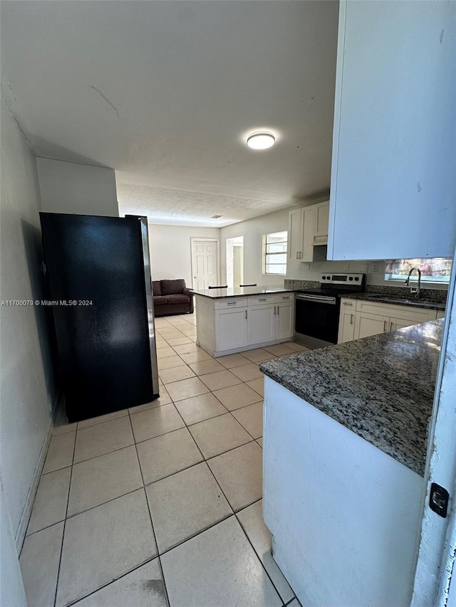 kitchen with kitchen peninsula, stainless steel electric range oven, fridge, light tile patterned flooring, and white cabinetry