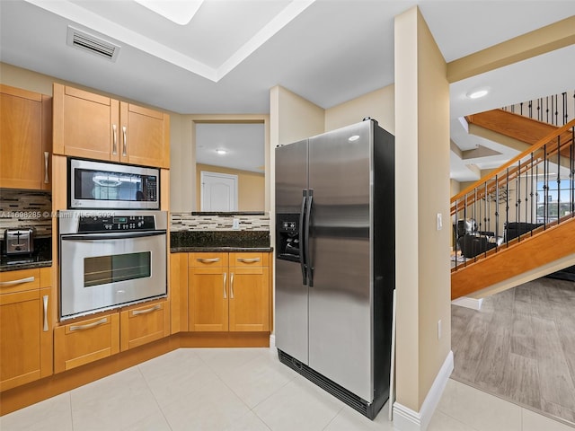 kitchen featuring dark stone countertops, backsplash, appliances with stainless steel finishes, and light hardwood / wood-style flooring