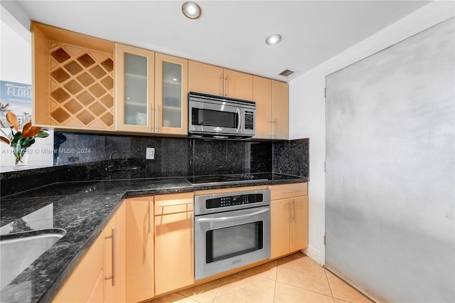 kitchen featuring appliances with stainless steel finishes, backsplash, light brown cabinetry, dark stone counters, and light tile patterned floors