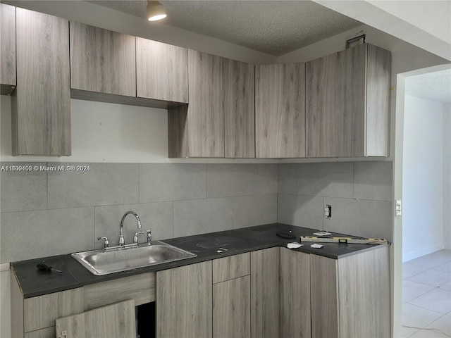 kitchen featuring decorative backsplash, a textured ceiling, light tile patterned flooring, and sink