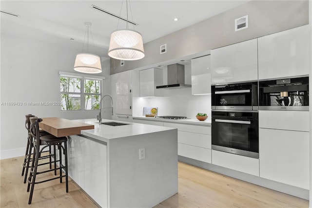 kitchen with a sink, visible vents, white cabinets, wall chimney exhaust hood, and modern cabinets