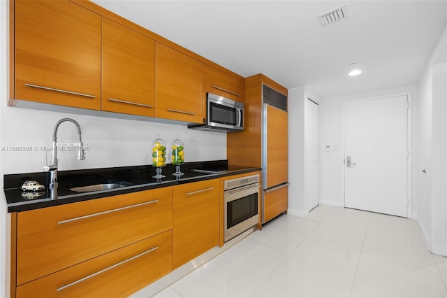 kitchen with sink, stainless steel appliances, dark stone countertops, and light tile patterned floors