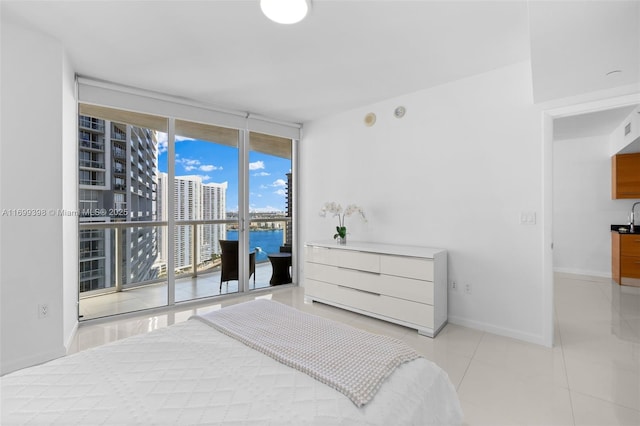 bedroom featuring access to outside, a water view, light tile patterned floors, a wall of windows, and sink