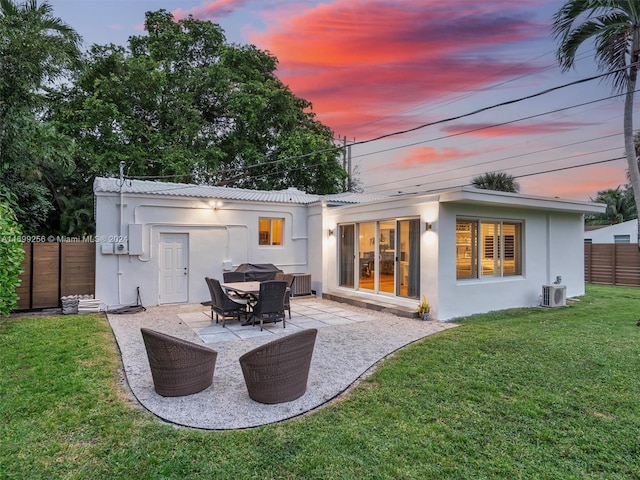 back house at dusk with a yard, cooling unit, and a patio area