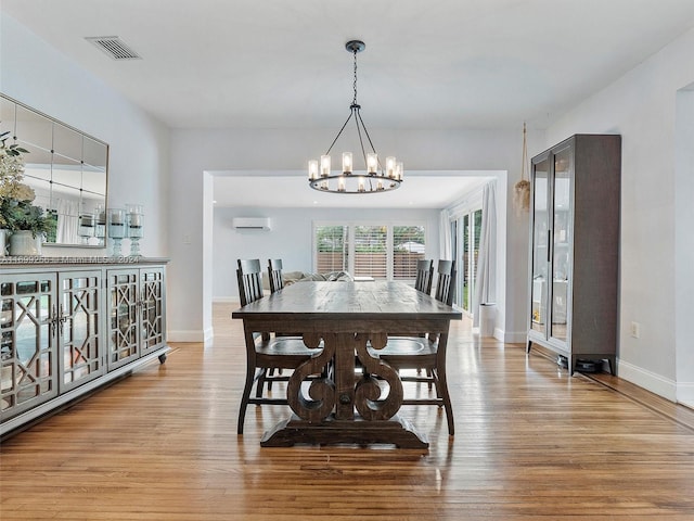 dining area with light hardwood / wood-style flooring, a chandelier, and a wall mounted air conditioner