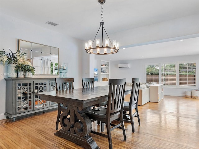 dining space with a wall mounted air conditioner, light hardwood / wood-style floors, and a chandelier