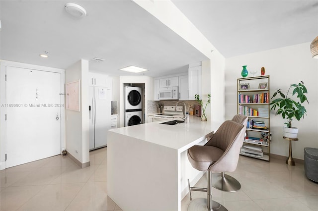 kitchen with white cabinetry, sink, kitchen peninsula, white appliances, and stacked washer and clothes dryer