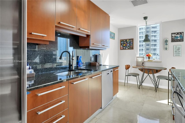 kitchen with dark stone counters, sink, hanging light fixtures, stainless steel fridge, and dishwashing machine