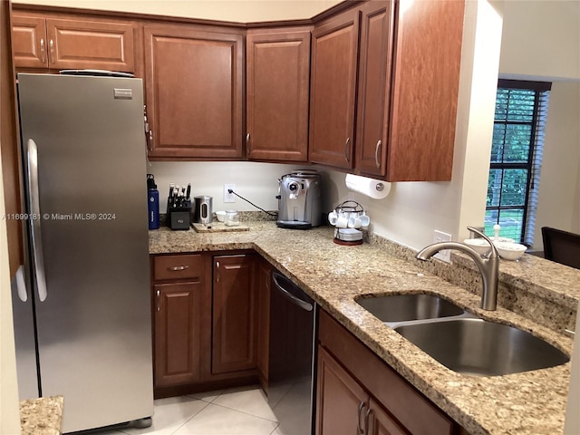 kitchen featuring stainless steel refrigerator, sink, black dishwasher, light stone counters, and light tile patterned floors