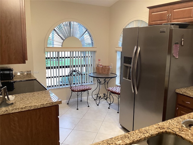 kitchen with stainless steel fridge, light stone counters, light tile patterned floors, and black stove