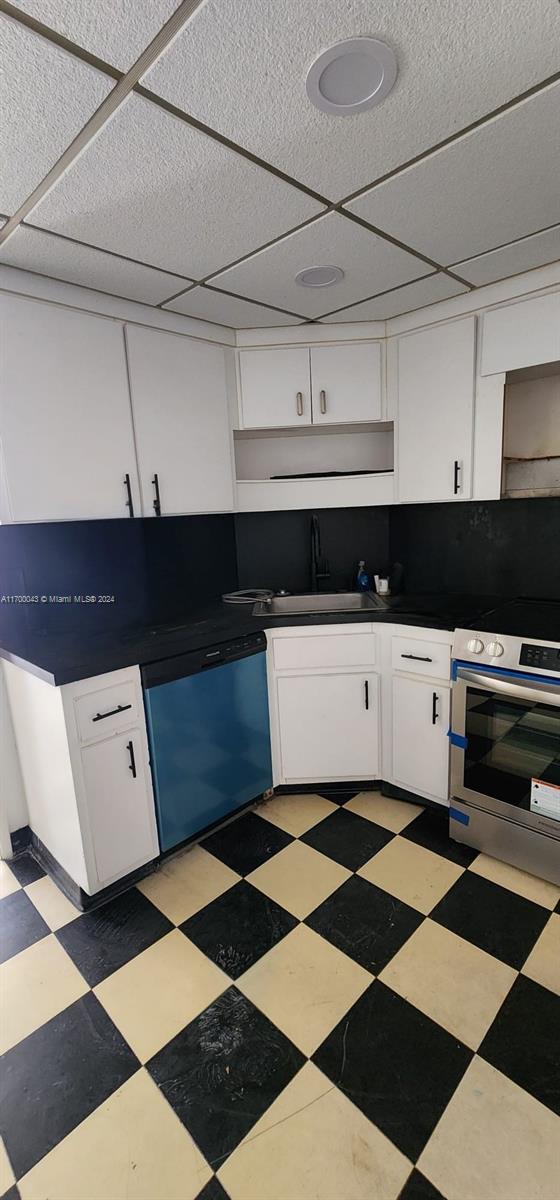 kitchen with appliances with stainless steel finishes, a paneled ceiling, white cabinetry, and sink