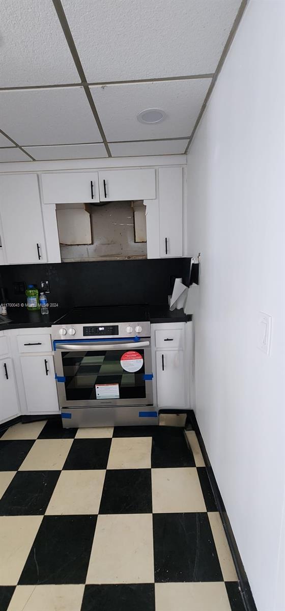 kitchen with white cabinets, a drop ceiling, and range