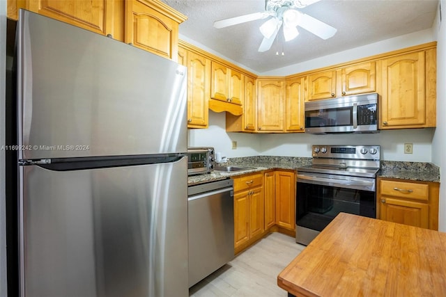 kitchen featuring ceiling fan, stainless steel appliances, wood counters, light hardwood / wood-style floors, and a textured ceiling