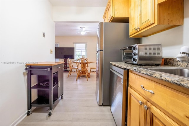 kitchen with light wood-type flooring, light stone counters, ceiling fan, sink, and dishwasher