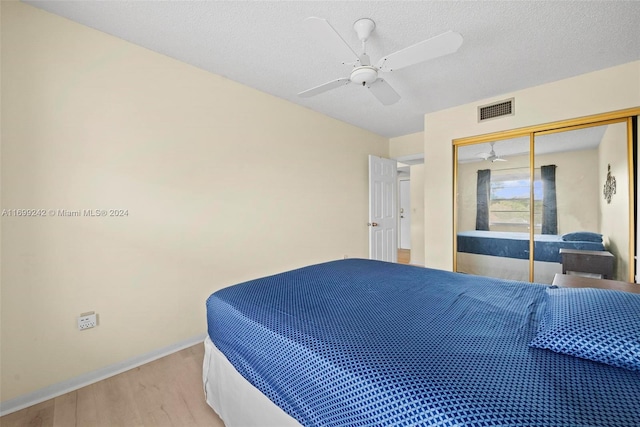 bedroom with ceiling fan, light hardwood / wood-style floors, a textured ceiling, and a closet