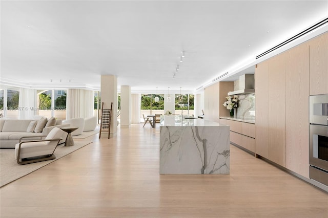 kitchen featuring rail lighting, light stone counters, light wood-type flooring, oven, and wall chimney range hood