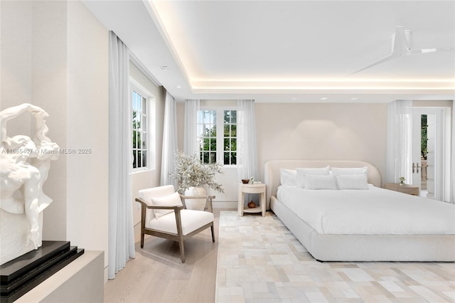 bedroom with light wood-type flooring and a tray ceiling