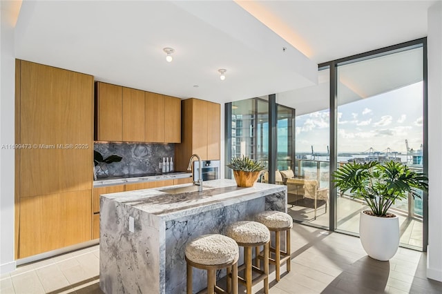 kitchen featuring sink, a water view, an island with sink, a wall of windows, and backsplash