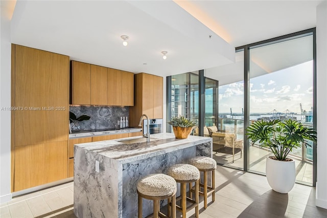 500 Alton Unit 2405/06, Miami Beach, FL 33139 - kitchen with a kitchen breakfast bar, brown cabinets, expansive windows, a sink, and light stone countertops
