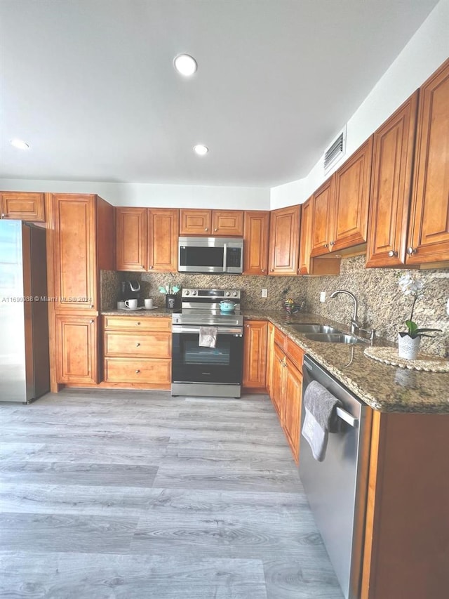 kitchen with decorative backsplash, appliances with stainless steel finishes, sink, light hardwood / wood-style flooring, and dark stone countertops