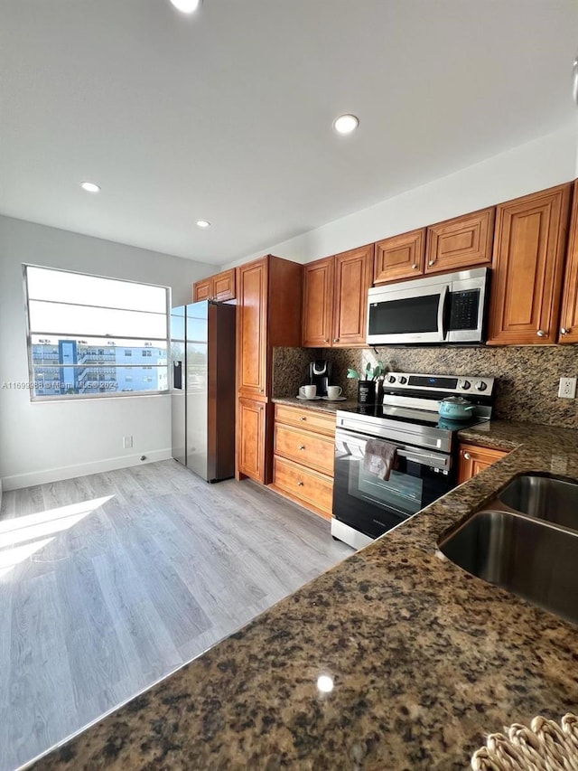 kitchen with sink, light hardwood / wood-style flooring, decorative backsplash, dark stone countertops, and appliances with stainless steel finishes