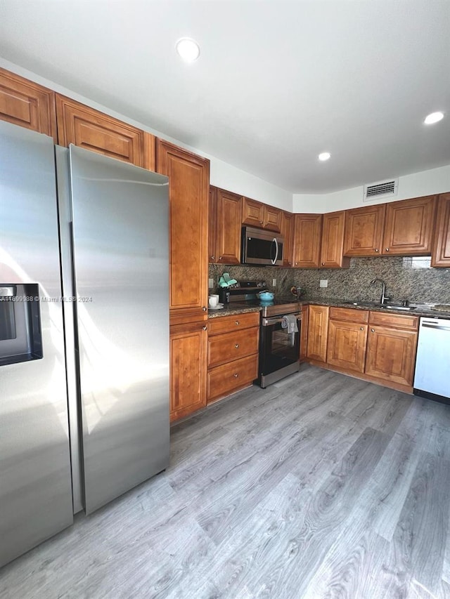 kitchen with dark stone counters, sink, decorative backsplash, light wood-type flooring, and appliances with stainless steel finishes