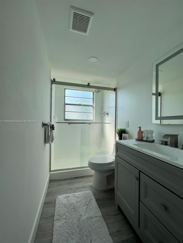 bathroom featuring hardwood / wood-style floors, vanity, toilet, and a shower with door