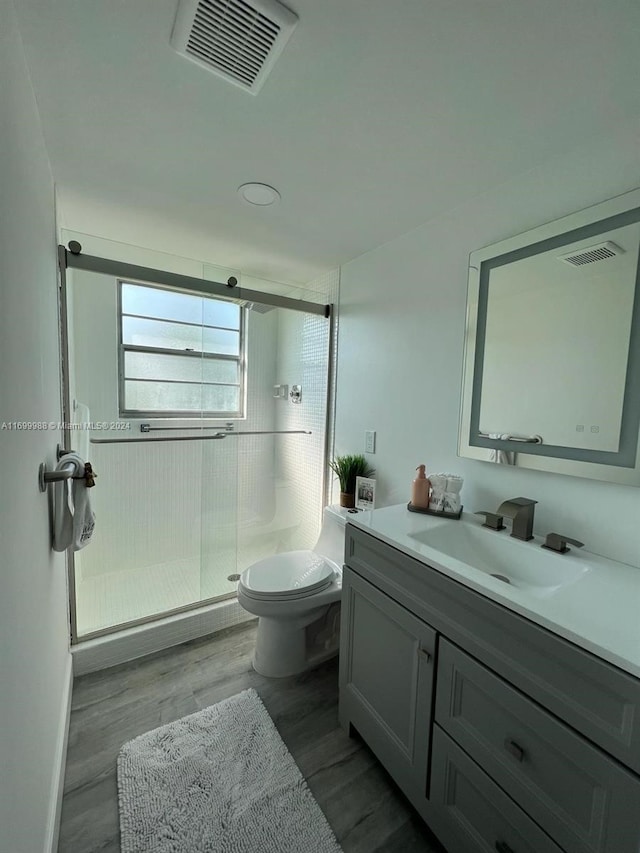 bathroom with hardwood / wood-style flooring, vanity, toilet, and a shower with door