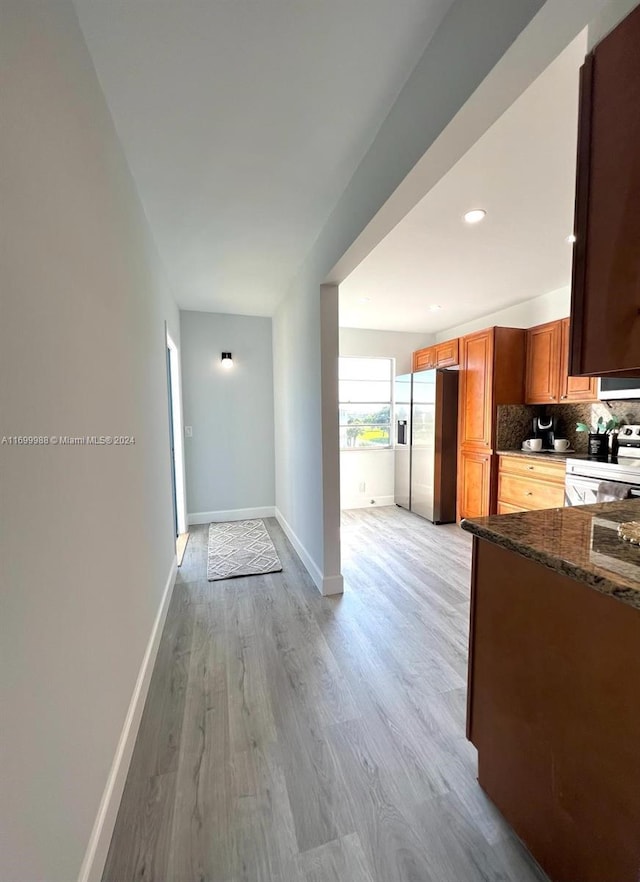 kitchen featuring tasteful backsplash, dark stone countertops, stainless steel appliances, and light wood-type flooring