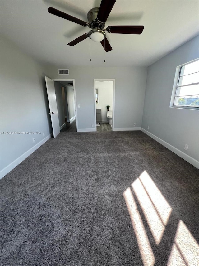 unfurnished bedroom with dark carpet, ensuite bath, and ceiling fan