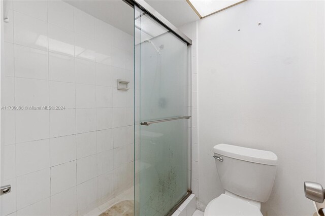 bathroom featuring a shower with door and toilet