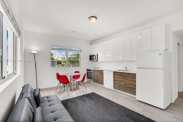 kitchen with stainless steel appliances, white cabinetry, light hardwood / wood-style floors, and sink