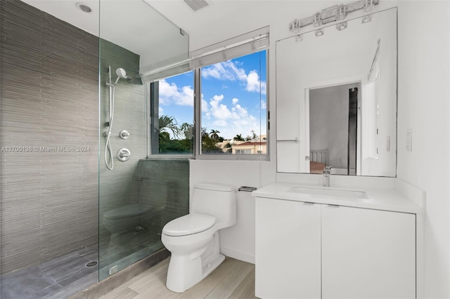 bathroom with hardwood / wood-style floors, vanity, a tile shower, and toilet