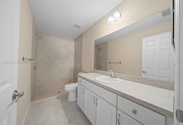 bathroom with tiled shower, tile patterned flooring, vanity, and toilet