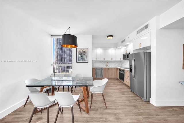 kitchen featuring white cabinets, decorative light fixtures, light hardwood / wood-style floors, and stainless steel appliances