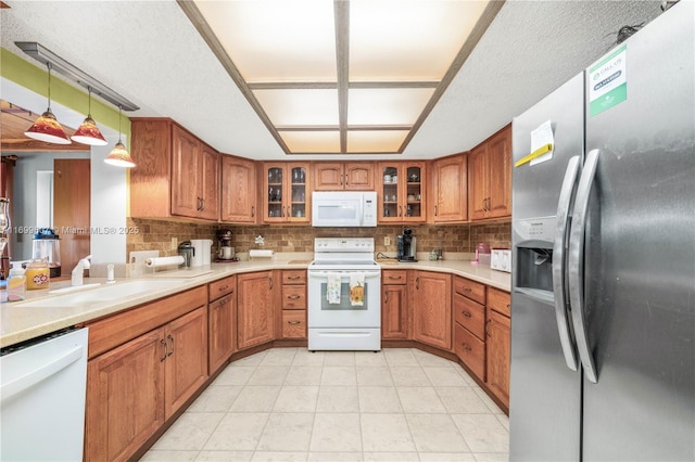 kitchen featuring a sink, decorative backsplash, white appliances, and brown cabinets