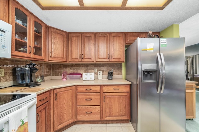 kitchen featuring glass insert cabinets, white appliances, brown cabinets, and light countertops