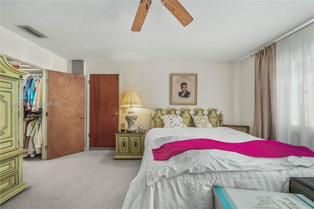 carpeted bedroom with visible vents, ceiling fan, a closet, a textured ceiling, and a walk in closet