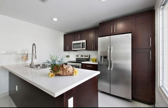 kitchen with kitchen peninsula, a kitchen bar, dark brown cabinets, stainless steel appliances, and sink