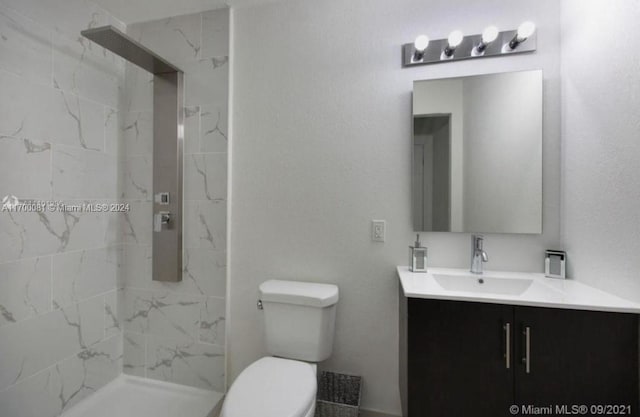 bathroom with a tile shower, vanity, and toilet