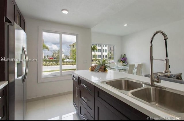 kitchen with dark brown cabinetry, stainless steel fridge, sink, and light tile patterned flooring