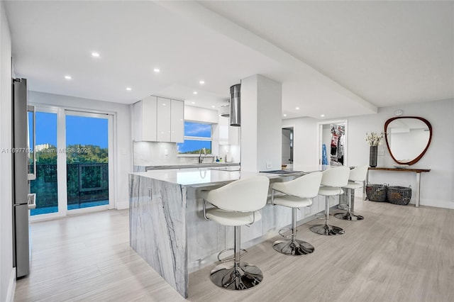 kitchen with stainless steel fridge, light hardwood / wood-style floors, decorative backsplash, white cabinetry, and a kitchen breakfast bar