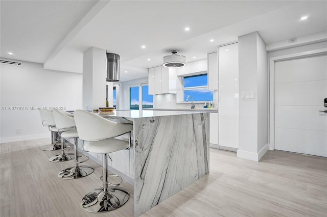 kitchen with decorative backsplash, light wood-type flooring, a breakfast bar area, white cabinetry, and sink