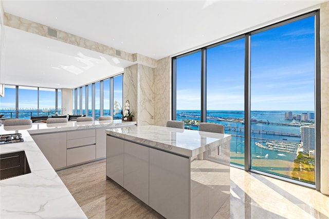 kitchen featuring a center island, a water view, light stone counters, expansive windows, and white cabinets