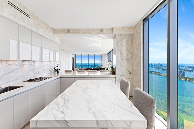 kitchen featuring white cabinetry, backsplash, a water view, light stone countertops, and stainless steel gas stovetop