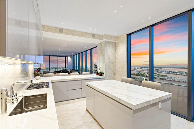 kitchen featuring a water view, expansive windows, white cabinets, a kitchen island, and stainless steel gas stovetop