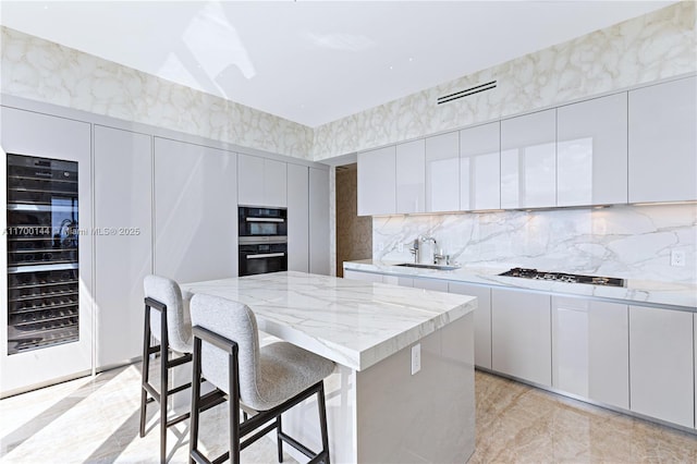 kitchen featuring sink, a breakfast bar area, a center island, black appliances, and white cabinets