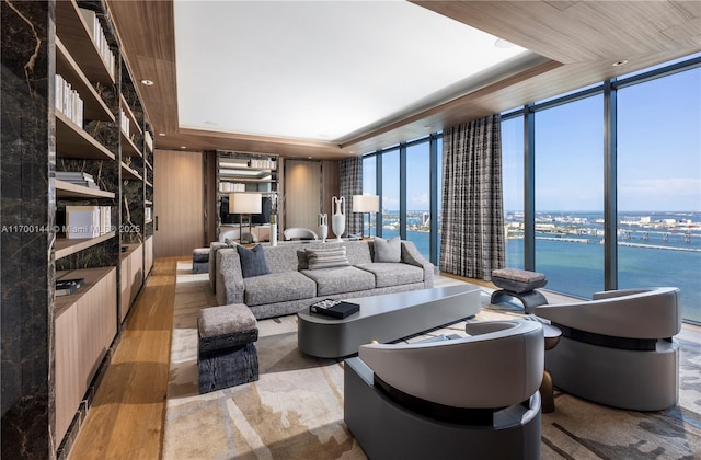 living room featuring a water view, expansive windows, a raised ceiling, and light wood-type flooring