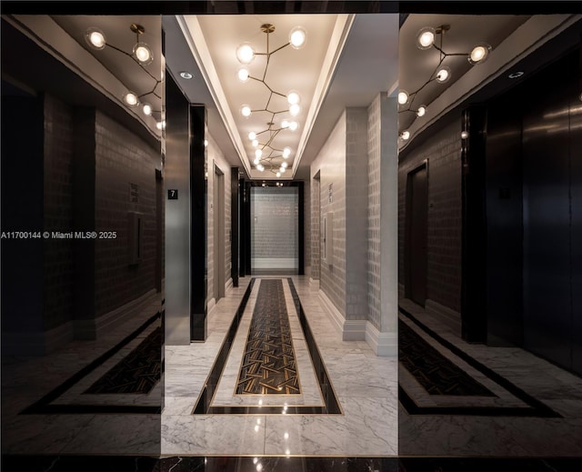 hallway with an inviting chandelier, ornamental molding, and a raised ceiling