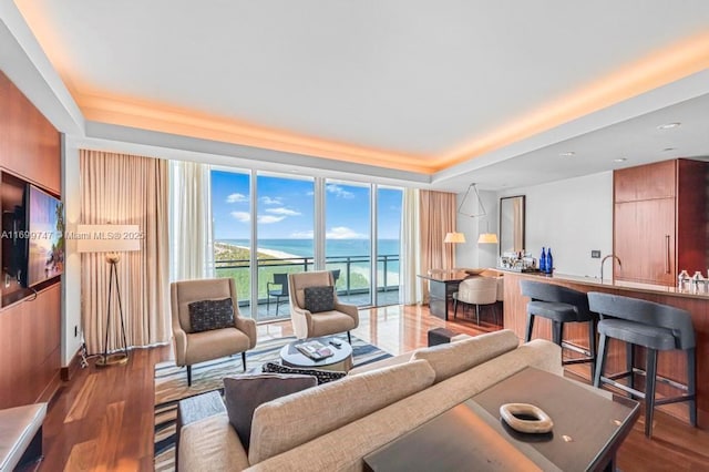 living room with hardwood / wood-style floors, a water view, a wall of windows, and sink